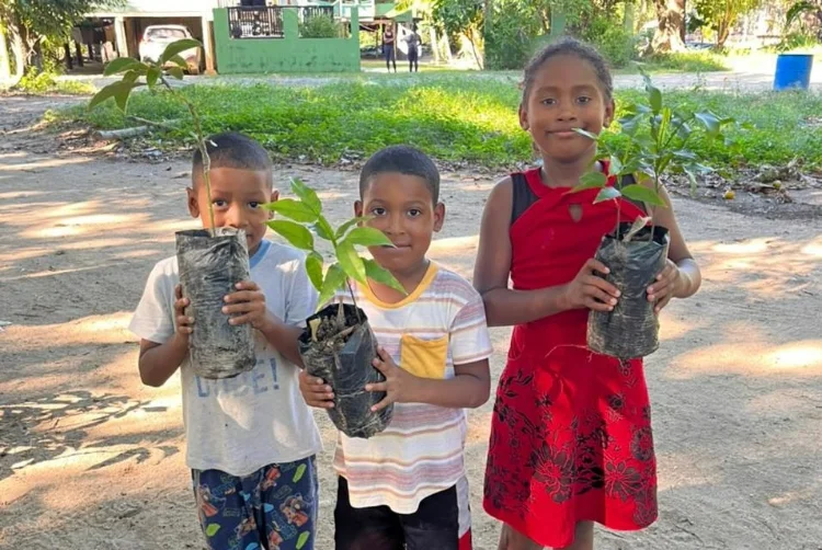 Honduran children hold life-saving fruit trees from the local regeneration hub.